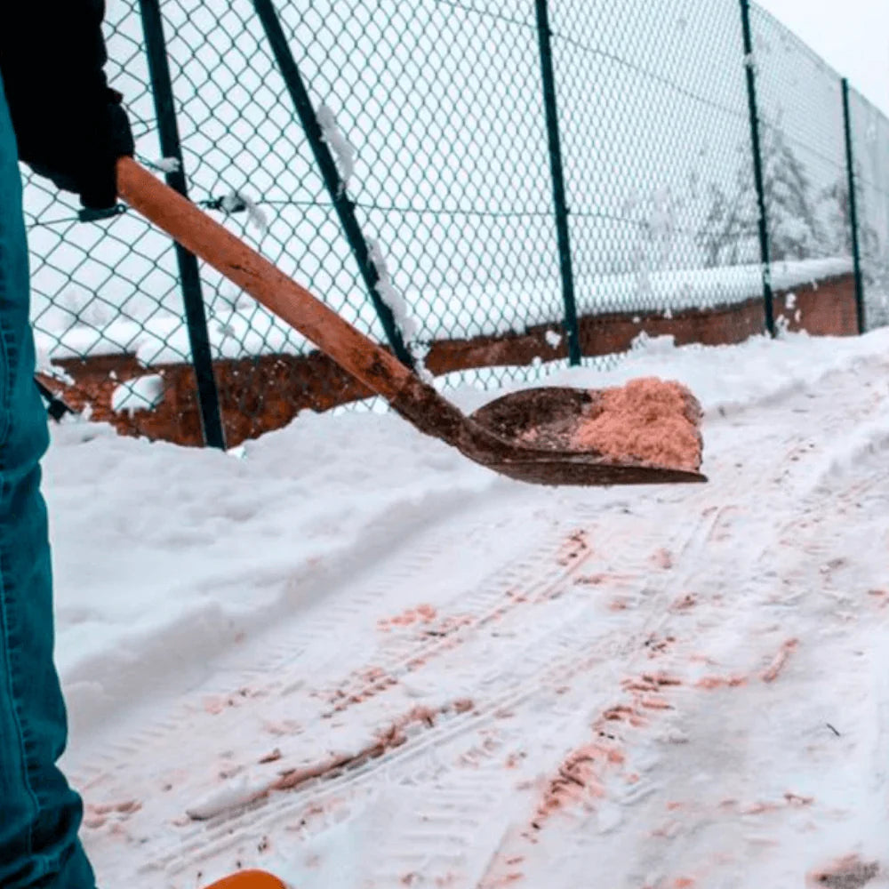 Person shoveling snow with a wooden shovel in a snowy outdoor setting.